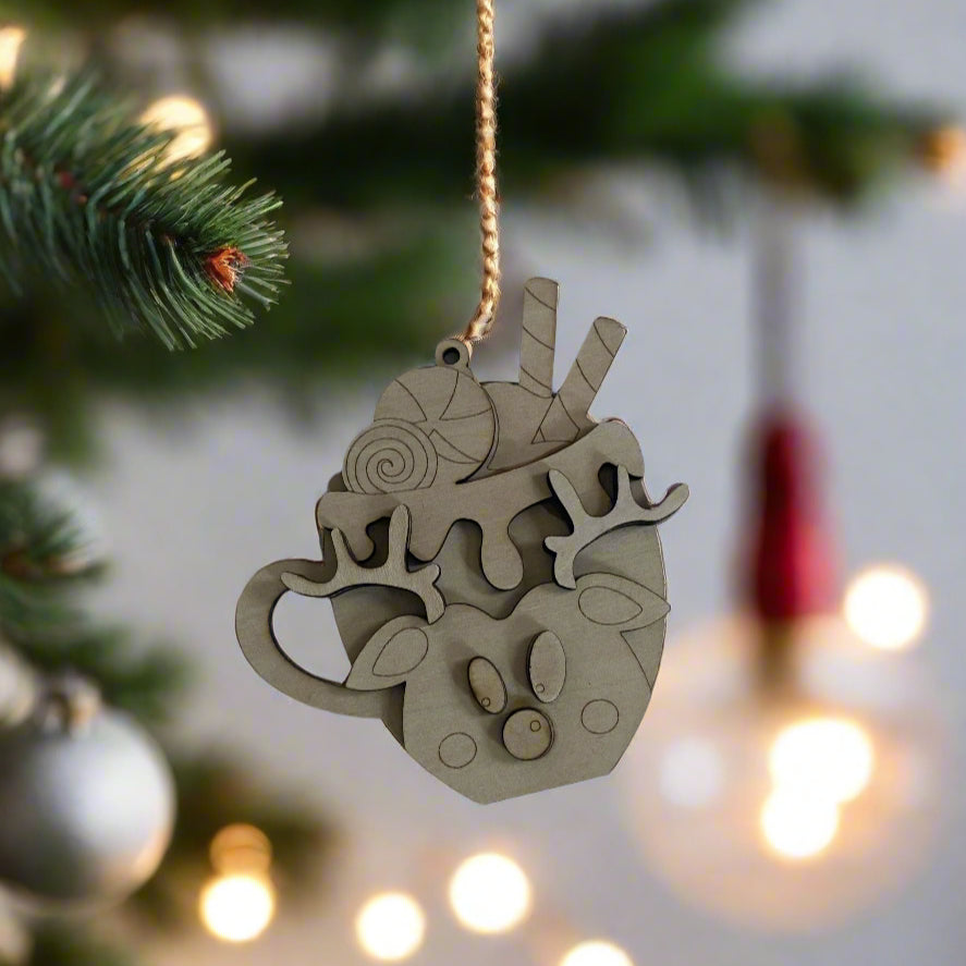 Decorative wooden ornament shaped like a teacup with Christmas elements hanging on a tree.